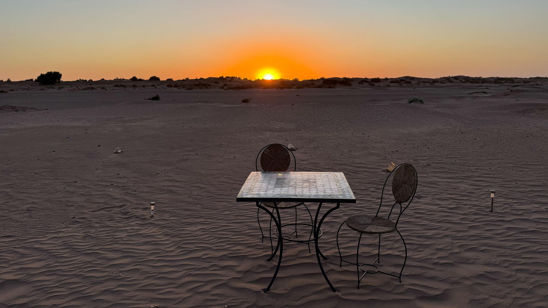 Image of a table and a chair in the Sahara desert at sunset