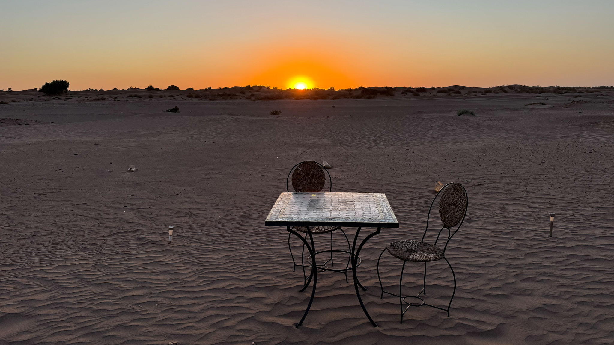 Bild mit Tisch und Stuhl im Sand der Sahara bei Sonnenuntergang