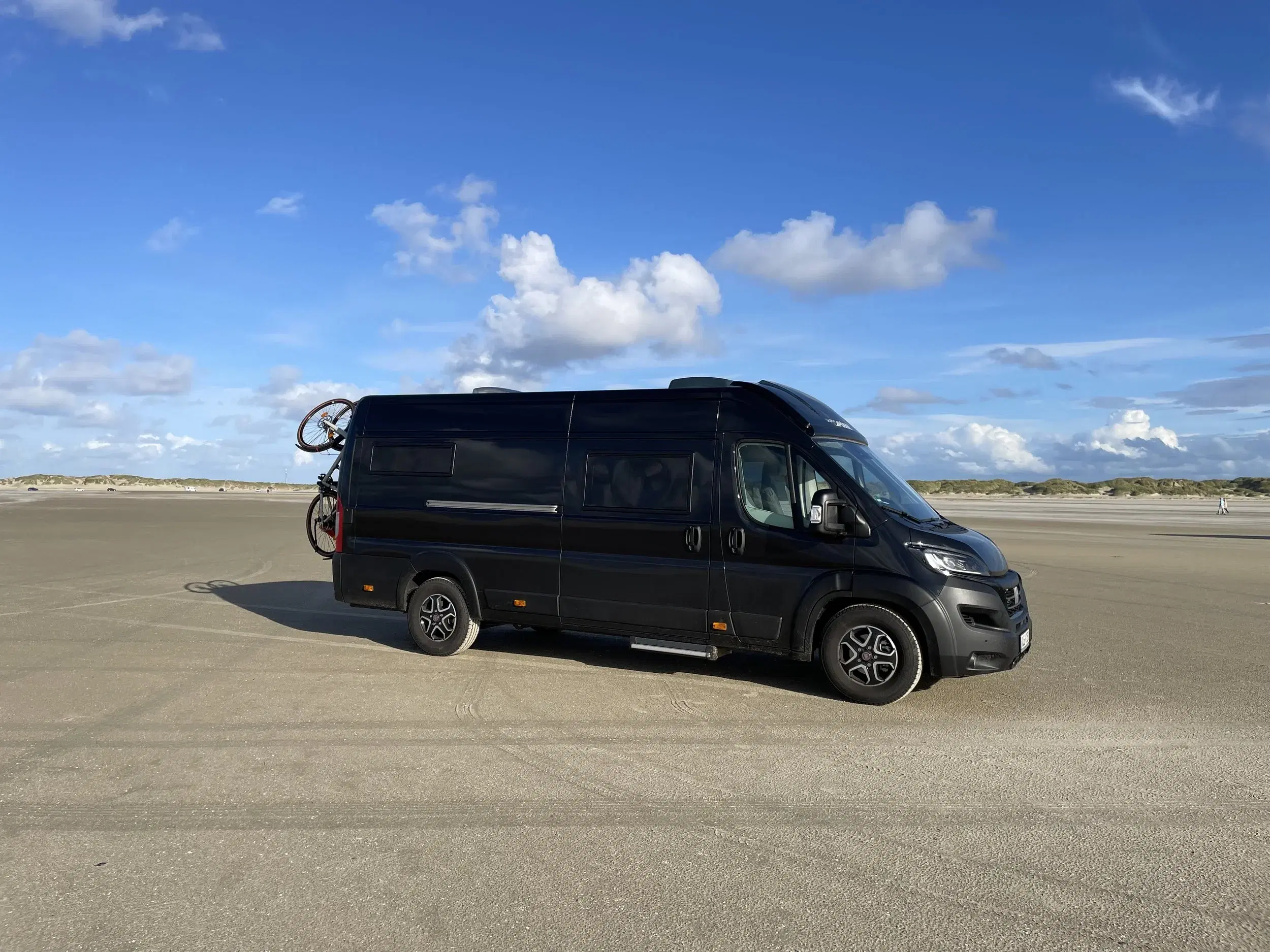 Image of our black campervan Wilma on a beach in Denmark.